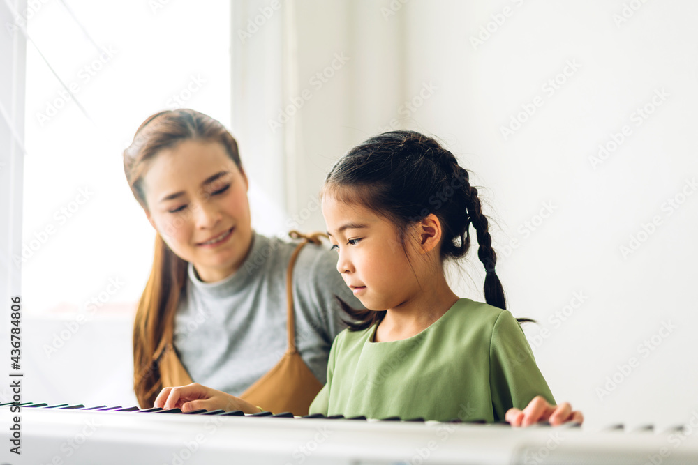 Portrait of enjoy happy love asian family mother and little asian girl child smiling and having fun teaching and play piano music lesson at home Portrait of enjoy happy love asian family mother and little asian girl child smiling and having fun teaching and play piano music lesson at home