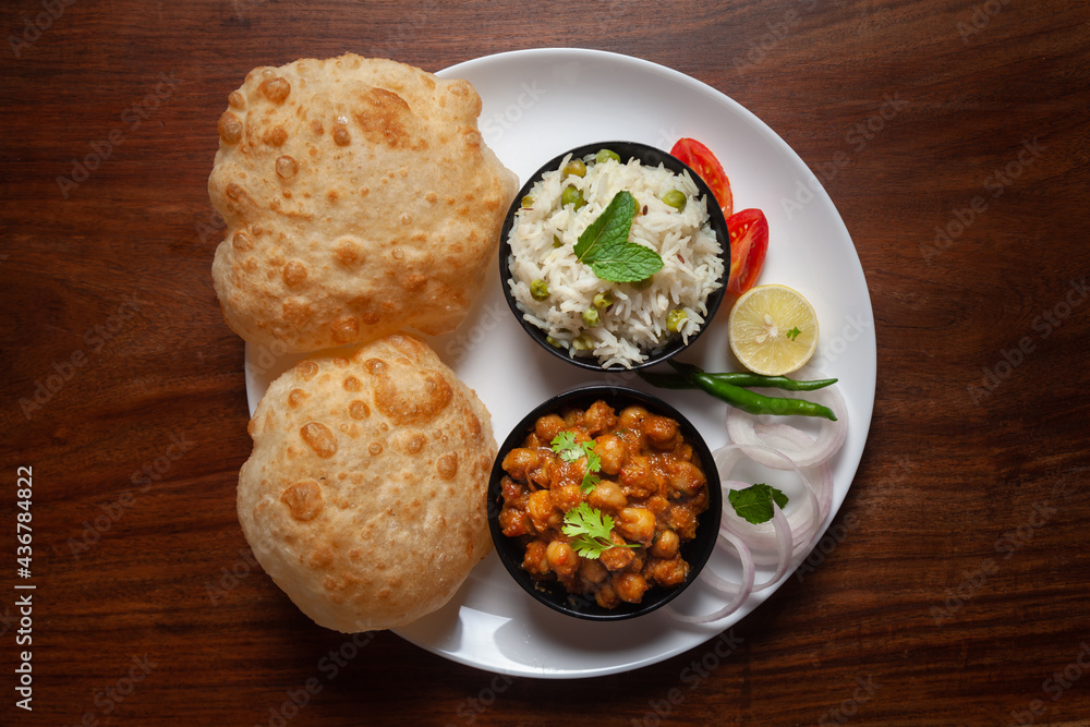 Chickpeas masala (Spicy chola or chhole curry) and Bhatura or Puri garnished with fresh green coriander and ingredients. A Classic Indian typical Panjabi street food. Chickpeas masala (Spicy chola or chhole curry) and Bhatura or Puri garnished with fresh green coriander and ingredients. A Classic Indian typical Panjabi street food.