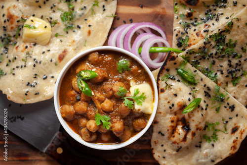 Close-up of fresh, hot tandoori roti or butter naan garnished with black till and green fresh coriander leaves and chole. A typical, traditional north indian panjabi food.