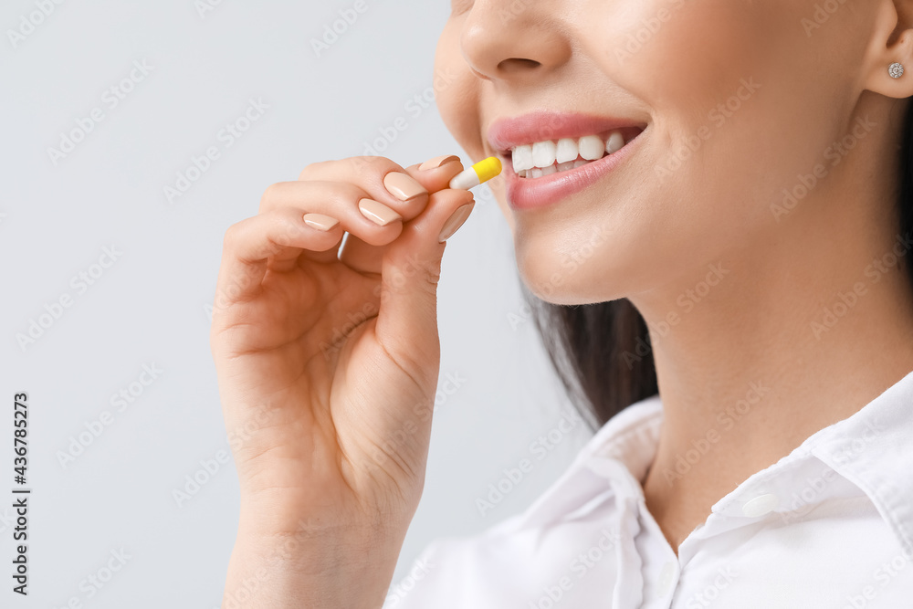 Beautiful young woman taking pills on light background, closeup Beautiful young woman taking pills on light background, closeup