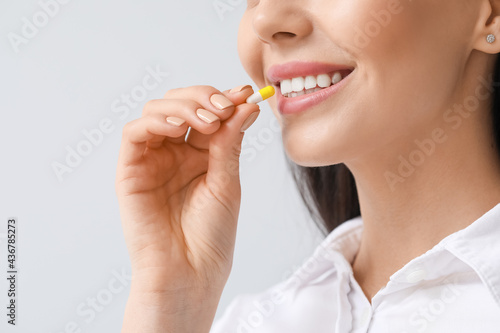 Beautiful young woman taking pills on light background, closeup