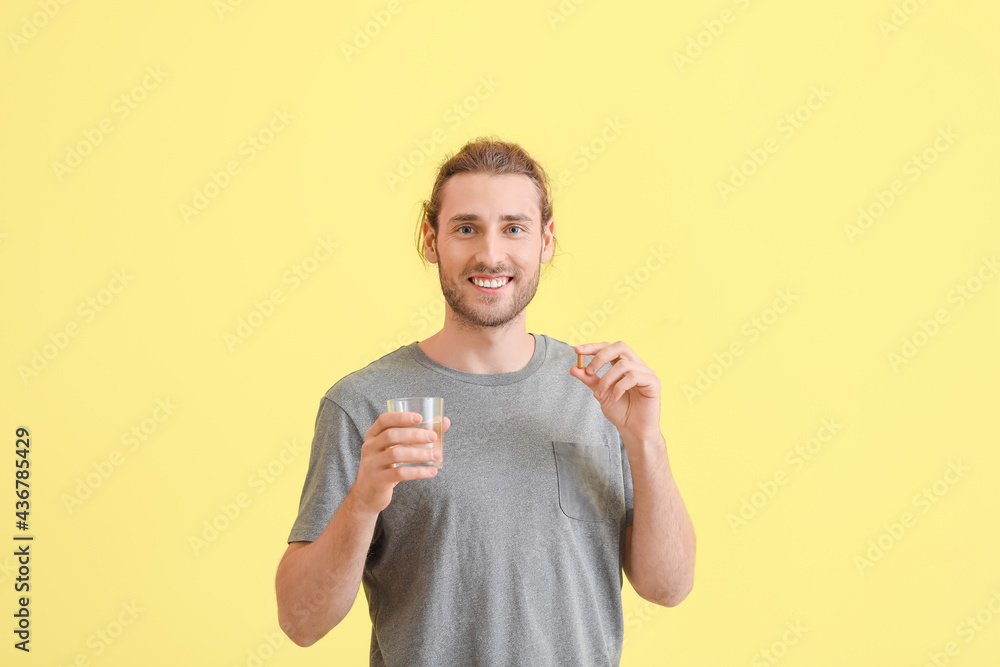 Handsome young man taking pills on color background Handsome young man taking pills on color background