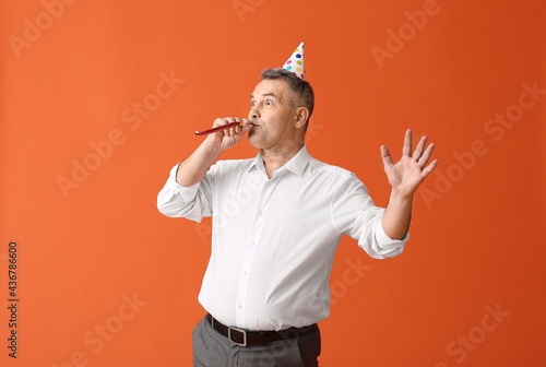 Happy mature man in party hat and with noisemaker on color background