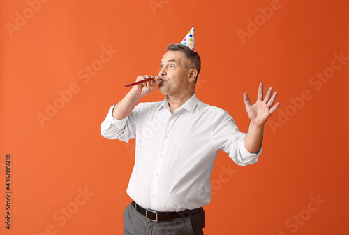 Happy mature man in party hat and with noisemaker on color background photo