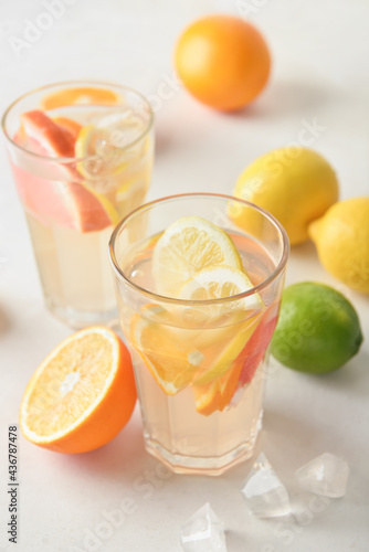 Glasses of tasty cold lemonade and citrus fruits on light background