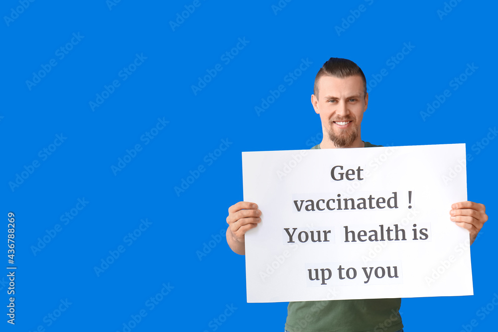Young man holding poster with text GET VACCINATED. YOUR HEALTH IS UP TO YOU on color background Young man holding poster with text GET VACCINATED. YOUR HEALTH IS UP TO YOU on color background