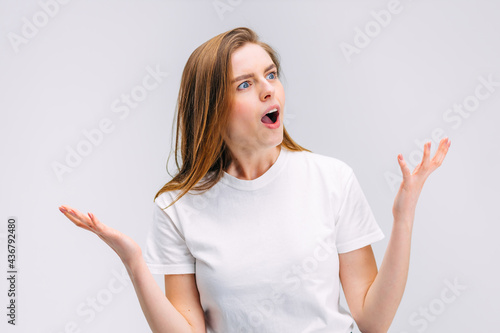 shocked woman with open mouth indignantly waves her hands on gray background.