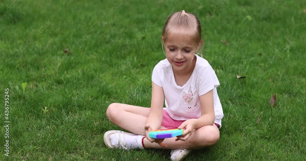 Child playing with rainbow pop it fidget toy outdoor. Push bubble sensory toy - washable and reusable silicon stress relief toy. Little girl plays with anti stress simple dimple toy. Child playing with rainbow pop it fidget toy outdoor. Push bubble sensory toy - washable and reusable silicon stress relief toy. Little girl plays with anti stress simple dimple toy.