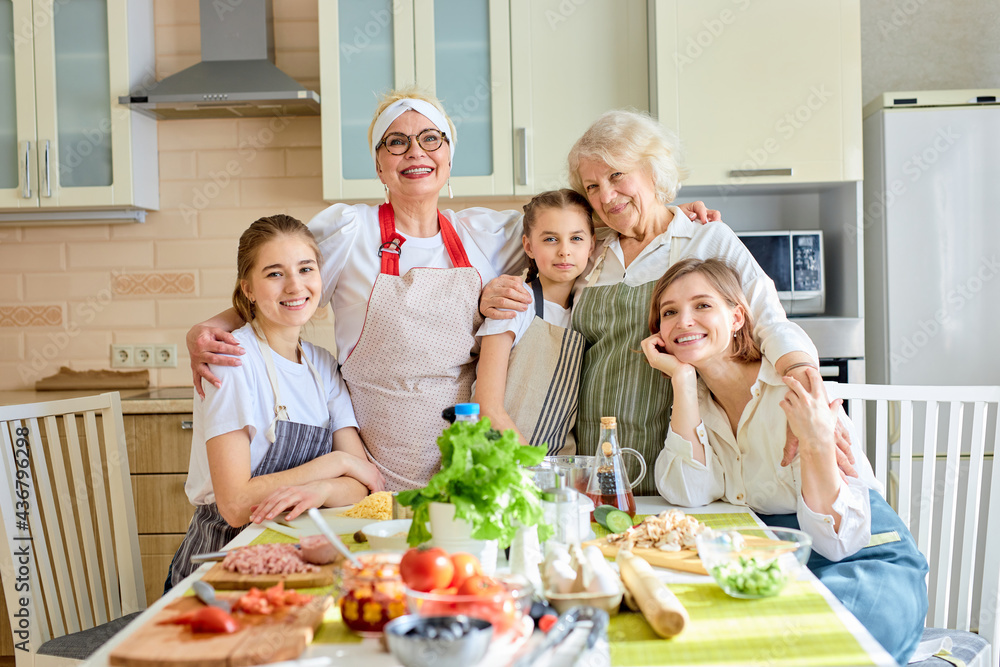 Portrait of smiling women children guhhing each other in bright cozy kitchen, posing at camera, spending ggod holidays together, wearing aprons. copy space
