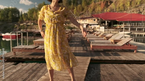Wallpaper Mural A young girl in a yellow dress is dancing barefoot alone on a wooden pier. There are wooden sun loungers on the pier. Torontodigital.ca