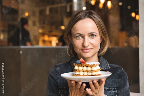 A beautiful caucasian woman holding and showing a plate with dessert in cafe. High quality photo