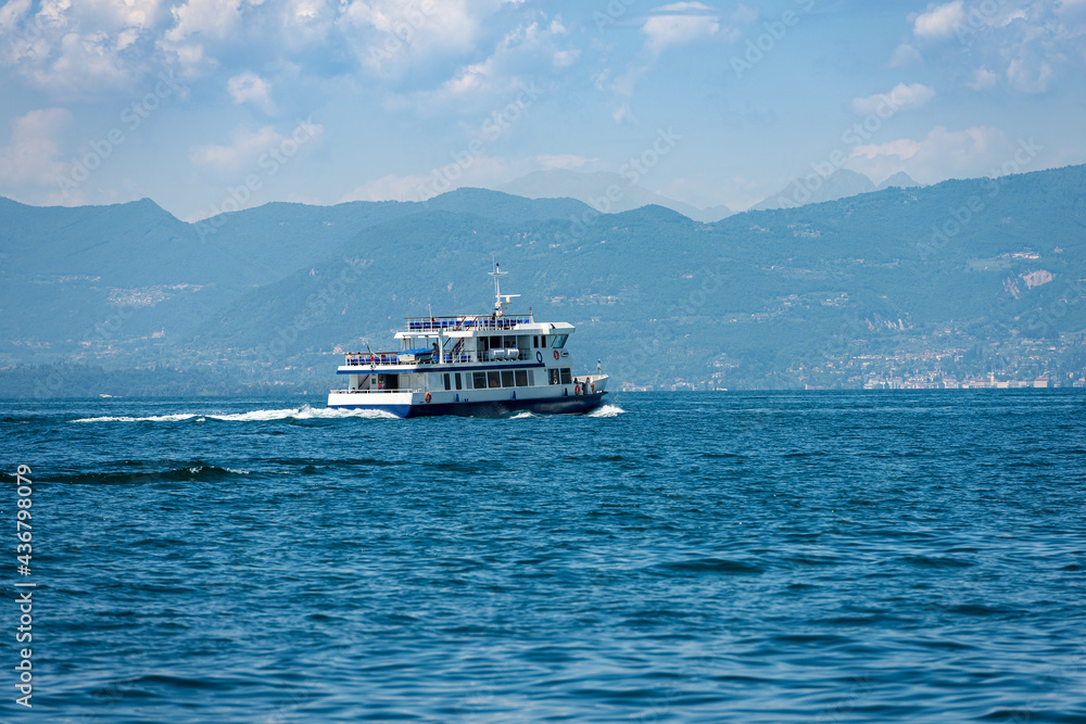 Ferry boat in motion in front of the small village of Bardolino on Lake Garda (Lago di Garda), Verona province, Veneto, Italy, Europe. On the horizon the coast of Lombardy with the mountains.
