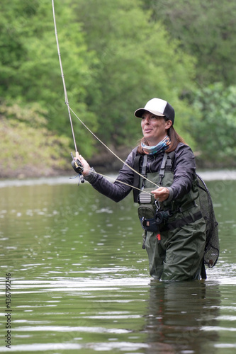 young woman fly fishing for trout in a clear river