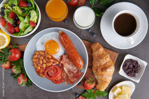 Delicious breakfast with fresh croissants, bacon, beans, sausage with fried egg, tomato and coffee served, milk, orange juice. strawberry, butterhead, blackberry salad. full american healthy breakfast