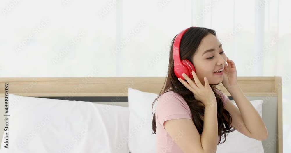 Young asian woman in pink shirt and singing along wearing red headphones looking happy Young asian woman in pink shirt and singing along wearing red headphones looking happy