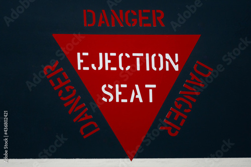 Red ejector seat warning sign triangle on jet fighter aeroplane fuselage. Danger alert message for ejection of pilot.