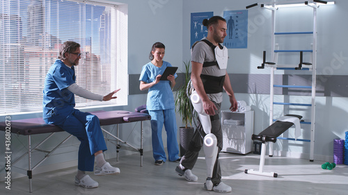 Man in exoskeleton learning to walk on treadmill near doctors photo