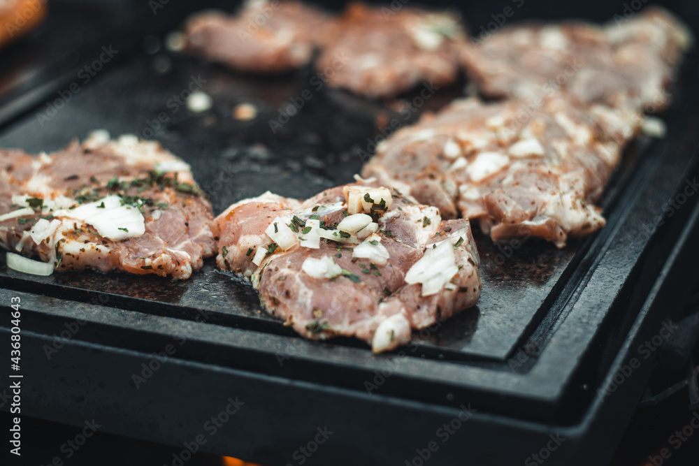 Preparation of pork neck pieces seasoned with basil, salt, olive oil, pepper, onion and garlic on a hot granite slab that receives heat from an open fire. The grilling season has begun