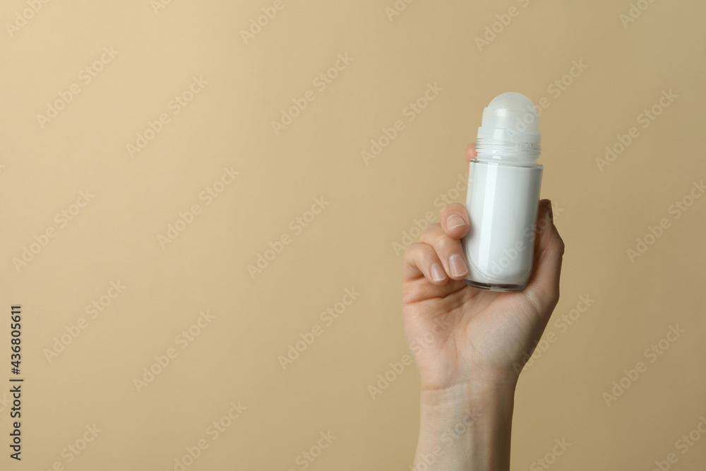 Female hand holds blank deodorant on beige background - obrazy, fototapety, plakaty 