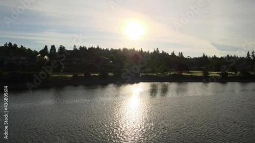 Gold sun over green trees, grass, and golden water reflection, at Lions Field Park Bremerton Kitsap County Washington State Pacific Northwest. Beautiful golden sunset over small town park. photo