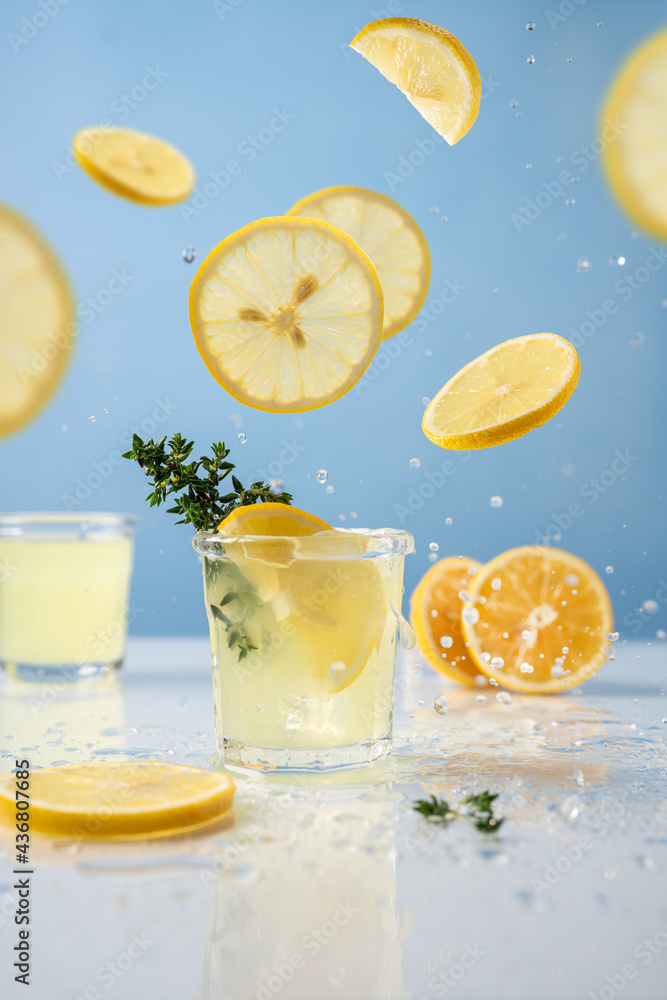 Limoncello in glass on blue background. Falling lemon slices and splashes. Summer background Limoncello in glass on blue background. Falling lemon slices and splashes. Summer background
