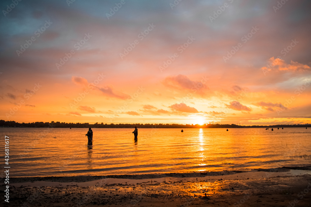 silhouettes of fishermen standing in the water and sunset