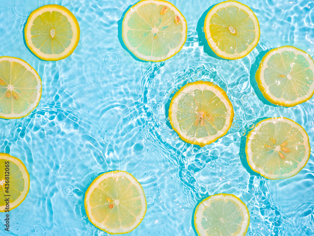 Lemon slices in clean transparent water over blue background with copy space. Water splashing on blue water surface in sunlight. Top view or flatlay. Summer, vacation, healthy eating concept Lemon slices in clean transparent water over blue background with copy space. Water splashing on blue water surface in sunlight. Top view or flatlay. Summer, vacation, healthy eating concept