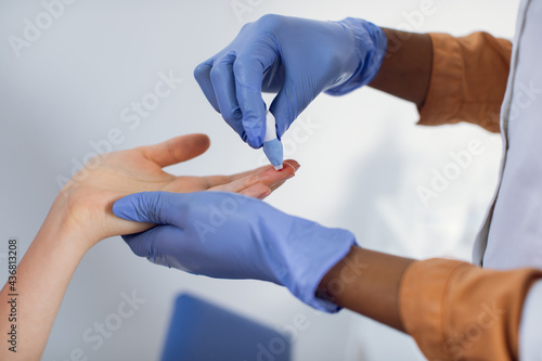 Close up cropped photo of hands of a female black nurse taking a patient's blood sample, using painless scarifier