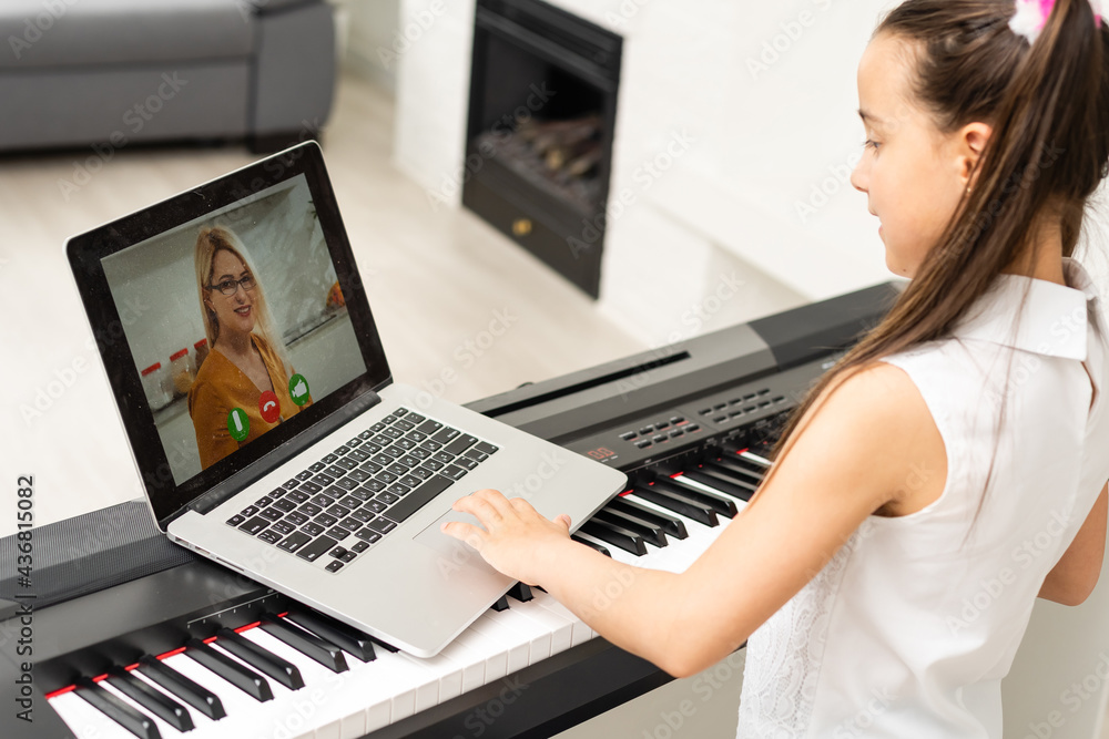 Fototapeta mała dziewczynka gra na pianinie w klasie edukacji z laptopem w domu nauka online w kwarantannie kryzysowej covid-19