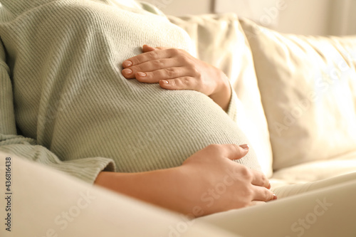 Pregnant young woman touching belly at home, closeup