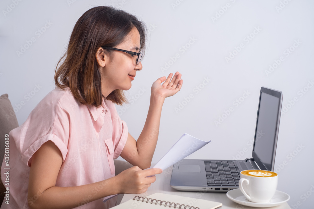bussiness woman or student wearing glasses sitting on sofa in living room looking talking at the compoter notebook or laptop. Stay and Work from home and student study and learn online at home office. bussiness woman or student wearing glasses sitting on sofa in living room looking talking at the compoter notebook or laptop. Stay and Work from home and student study and learn online at home office.