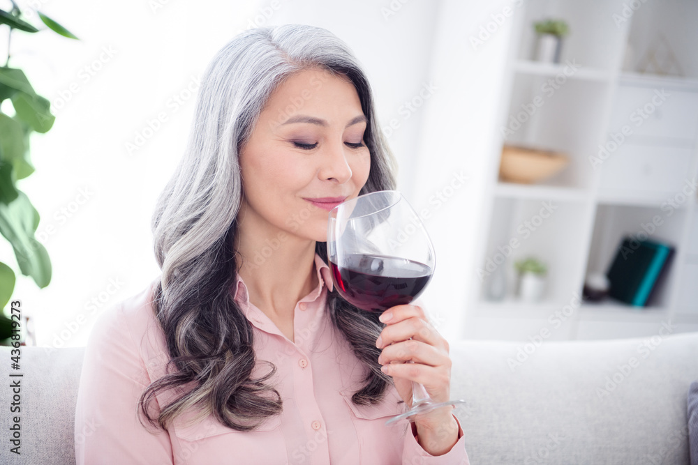 Photo of pretty satisfied person sit on couch hand hold smell big glass of wine spend free time house indoors Photo of pretty satisfied person sit on couch hand hold smell big glass of wine spend free time house indoors