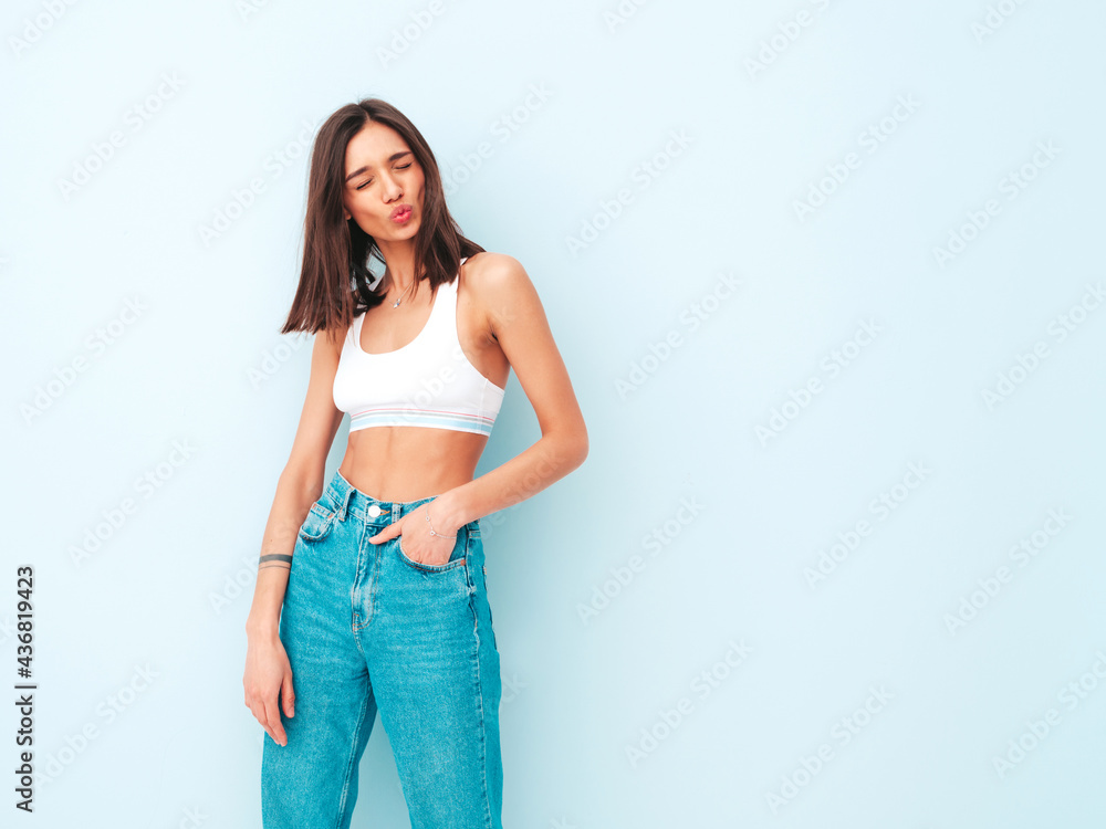 Beautiful smiling woman dressed in white jersey top shirt and jeans. Sexy carefree cheerful model enjoying her morning. Adorable and positive female posing near light blue wall in studio Beautiful smiling woman dressed in white jersey top shirt and jeans. Sexy carefree cheerful model enjoying her morning. Adorable and positive female posing near light blue wall in studio