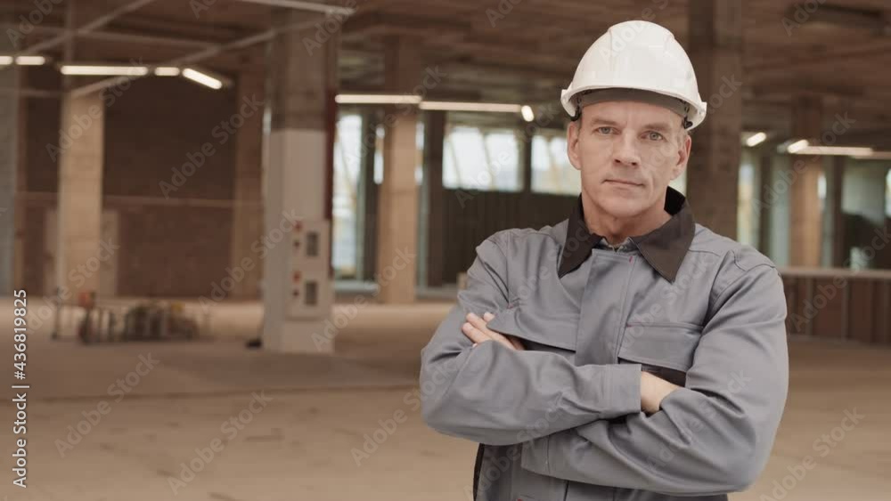 Waist-up POV of confident Caucasian foreman worker standing at construction site, crossing arms on chest and looking on camera Waist-up POV of confident Caucasian foreman worker standing at construction site, crossing arms on chest and looking on camera