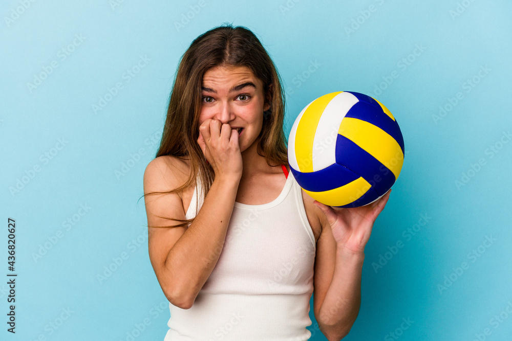 Young caucasian woman playing volleyball isolated on blue background biting fingernails, nervous and very anxious.