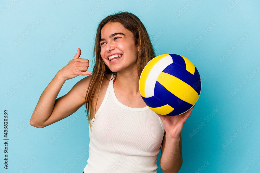 Young caucasian woman playing volleyball isolated on blue background showing a mobile phone call gesture with fingers.