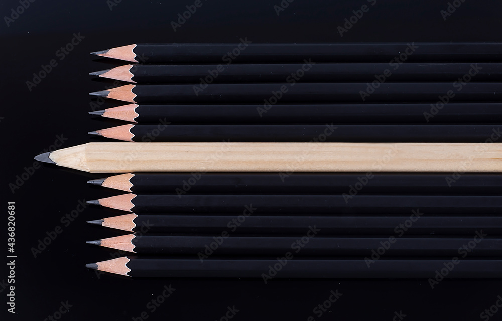 One white pencil standing out from the row of black pencils One white pencil standing out from the row of black pencils