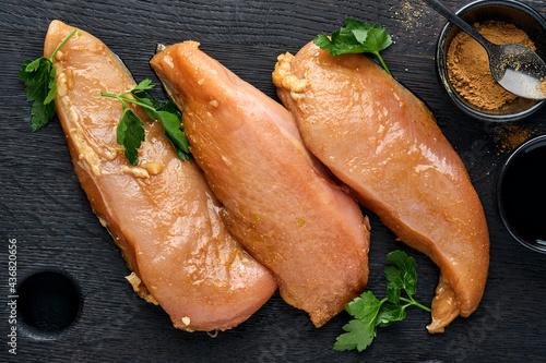 Foto Raw chicken meat fillet marinated in teriyaki soy sauce, onions, garlic and pepper in black plate on a dark slate, stone or concrete background