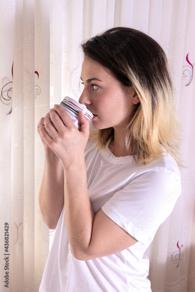 young woman drinking coffee in her room looking out the window young woman drinking coffee in her room looking out the window