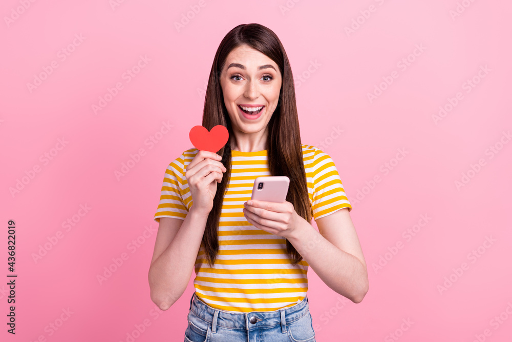 Photo of impressed young teen lady hold telephone heart wear orange t-shirt isolated on pink color background Photo of impressed young teen lady hold telephone heart wear orange t-shirt isolated on pink color background