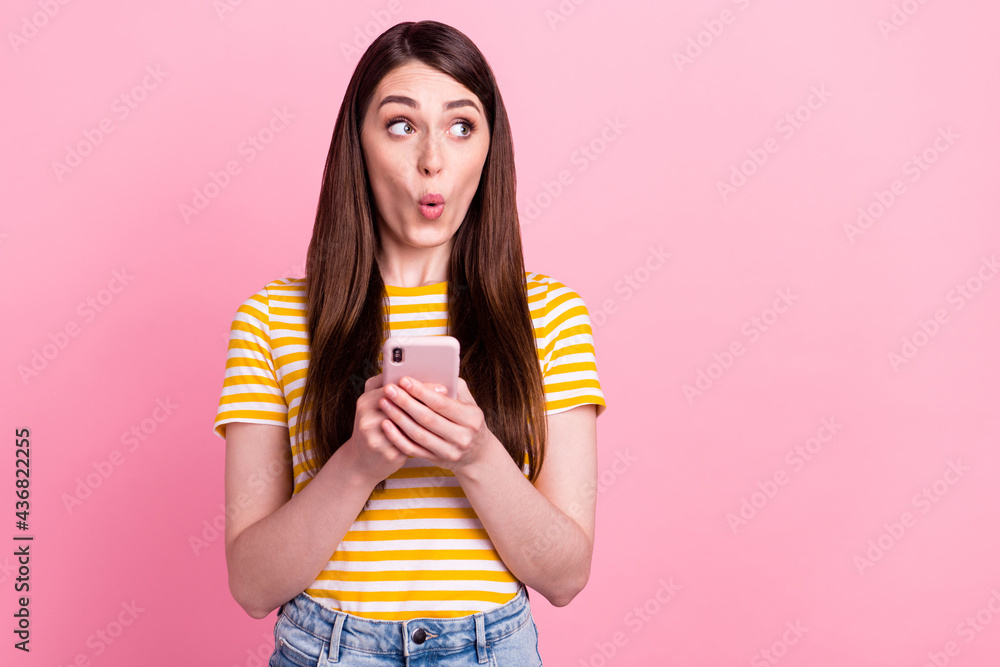 Photo of astonished young teen lady look empty space hold telephone wear orange t-shirt isolated on pink color background Photo of astonished young teen lady look empty space hold telephone wear orange t-shirt isolated on pink color background