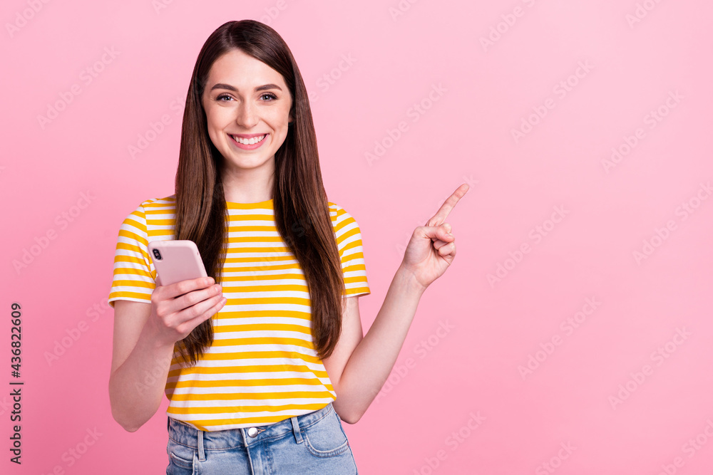 Photo of funny young millennial lady point empty space hold telephone wear orange t-shirt isolated on pastel pink color background Photo of funny young millennial lady point empty space hold telephone wear orange t-shirt isolated on pastel pink color background