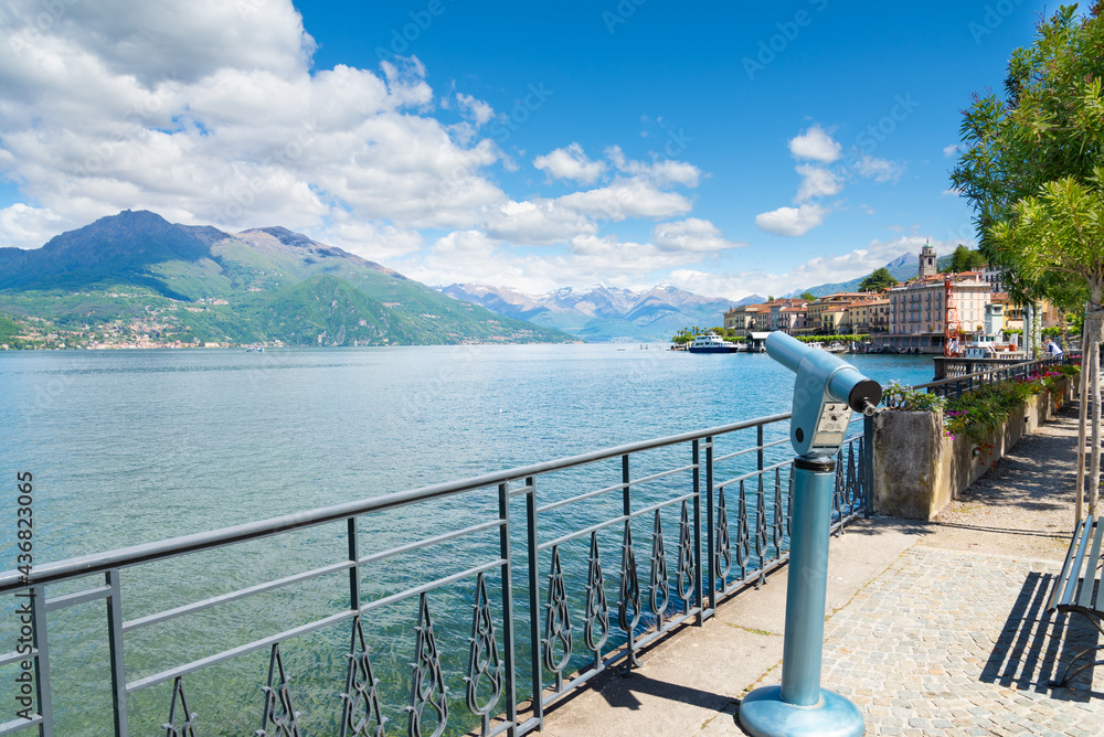A public telescope on the beautiful pedestrian promenade of Bellagio, Lake Como, Italy, with turquoise waters. Montains and blue sky on the background.