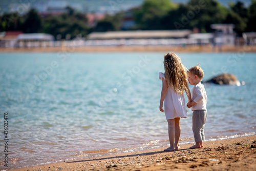 little boy and girl stand in the summer on the seashore, hold hands. Brother and sister in natural clothes. Tourism, vacations, vacations, traveling with children, sun protection and safety © katyagorphoto