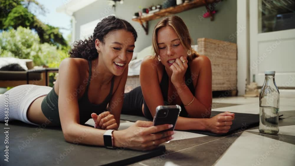 Mixed race friends lying on gym mat scrolling on cellular device finding a good workout to do at home Mixed race friends lying on gym mat scrolling on cellular device finding a good workout to do at home