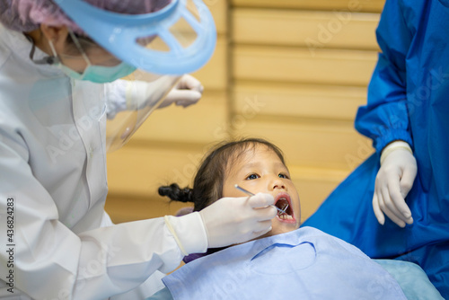 Dentist with face mask checking up Asian girl teeth with a mouth mirror and dental excavator in Dental office. Dental care  Medical care  Lifestyle  Dental clinic or dental procedure concepts
