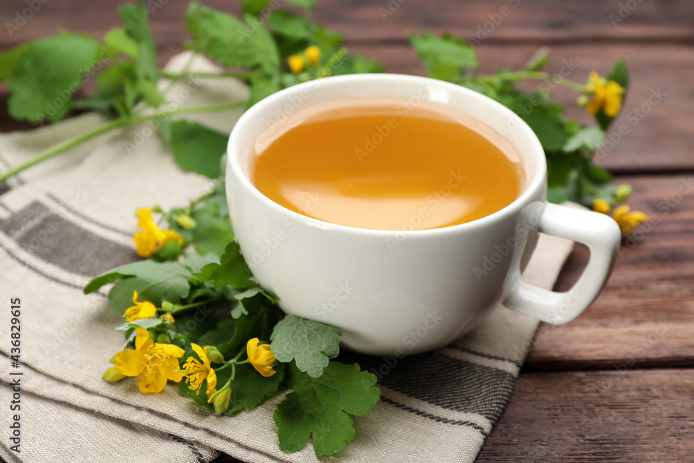 Cup of aromatic celandine tea and flowers on wooden table, closeup Cup of aromatic celandine tea and flowers on wooden table, closeup