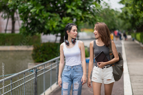 Two happy Asian students talking while walking in campus