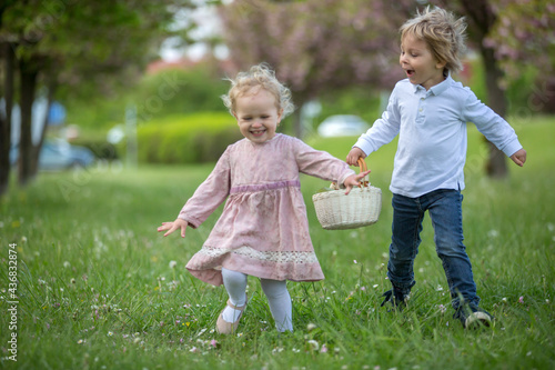 Beautiful children, toddler boy and girl, playing together in cherry blossom garden, running together and smiling with joy. Kids friendship