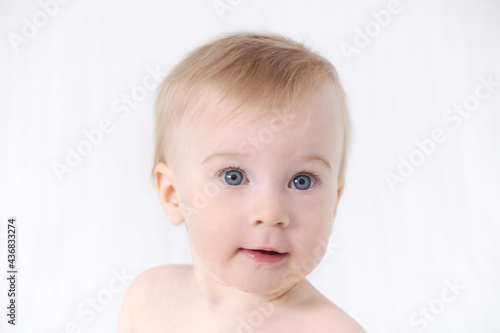 Close-up of cute little adorable funny caucasian blonde topless baby girl or boy on white  light grey background  looking at camera.Healthy skin.Happy childhood concept
